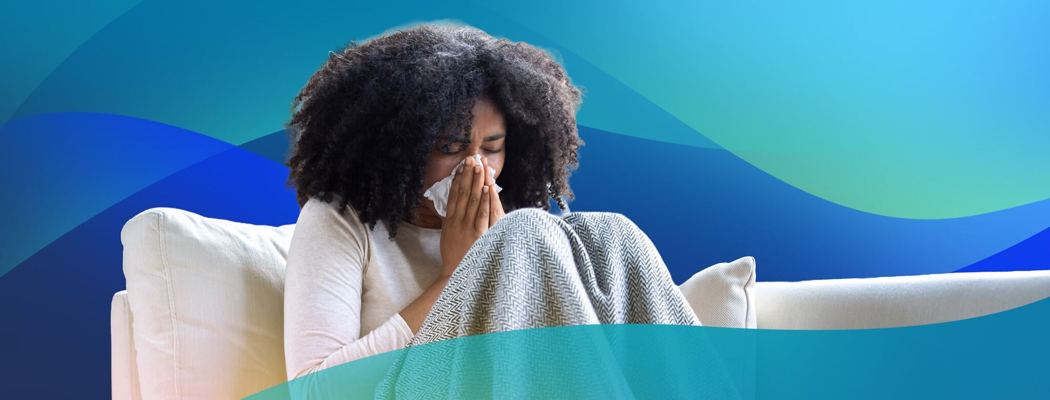 A woman on the couch blows her nose with a tissue.